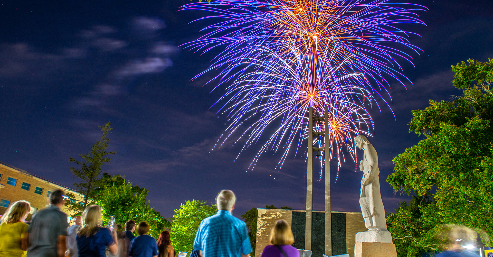 MSJ faculty and staff gathered in quad next to St. Joseph Statue watching beautiful fireworks in evening sky,