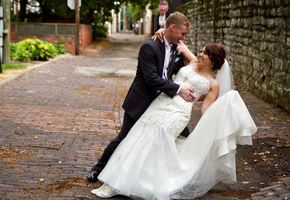 emily and tony knox in wedding attire on cobblestone street smiling at each other.