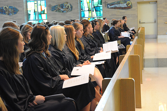 graduates in mater dei chapel pews holding programs.