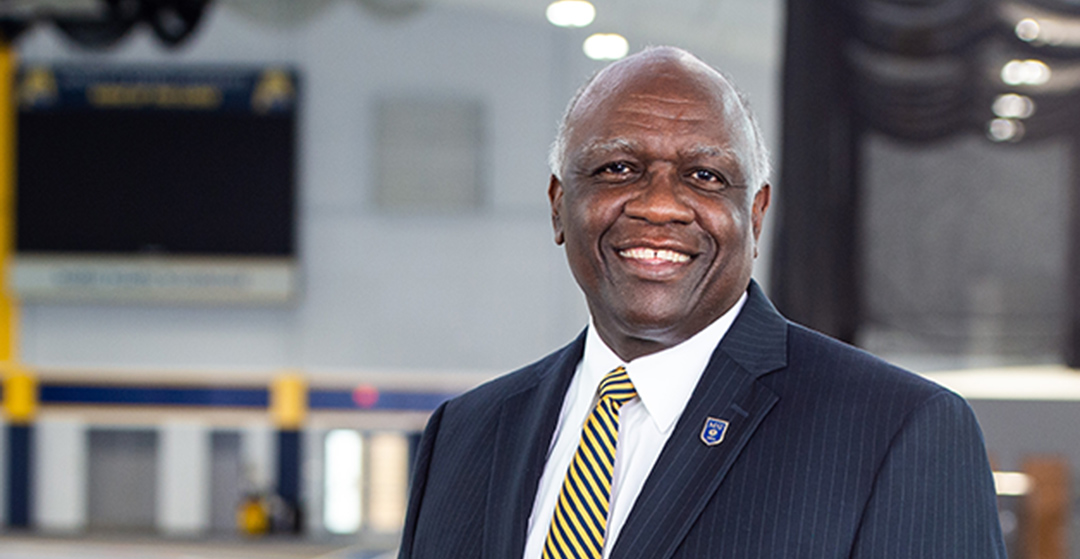 president H. James Williams standing and smiling in front of centennial fieldhouse indoor track