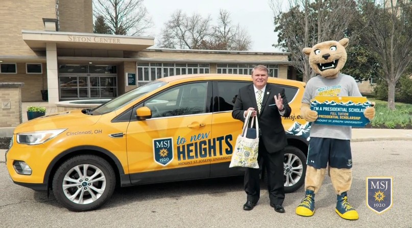 man standing by car with msj mascot